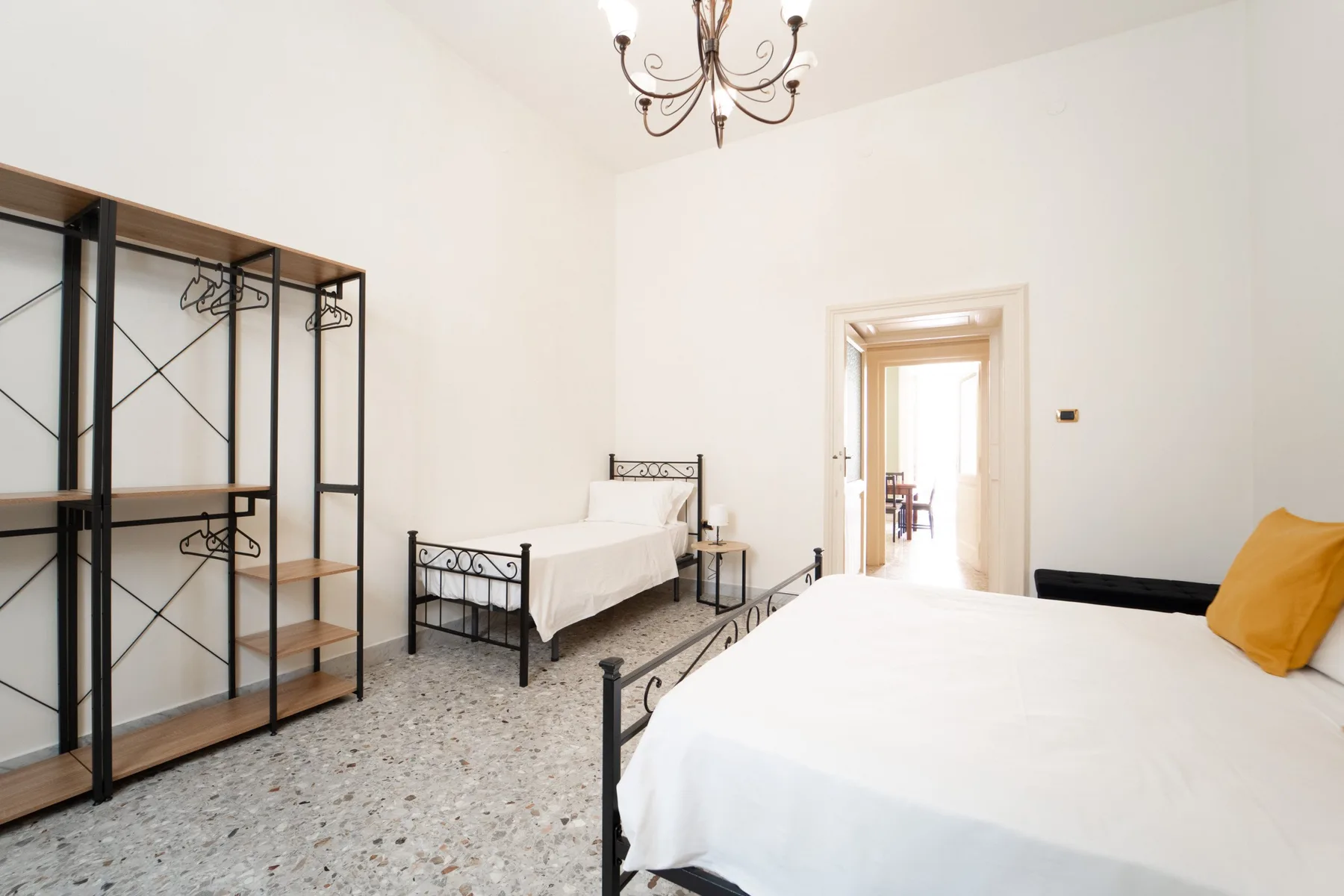 A bright bedroom with two beds and open shelving along the wall.