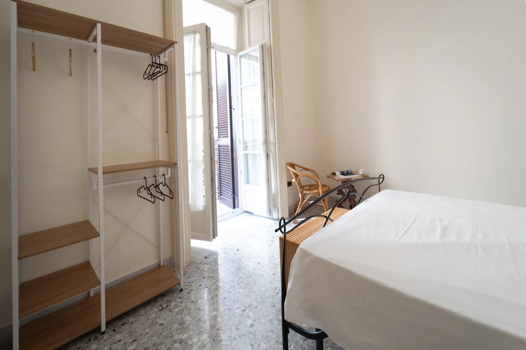 A bright bedroom with a bed beside an open window and clothing rack.