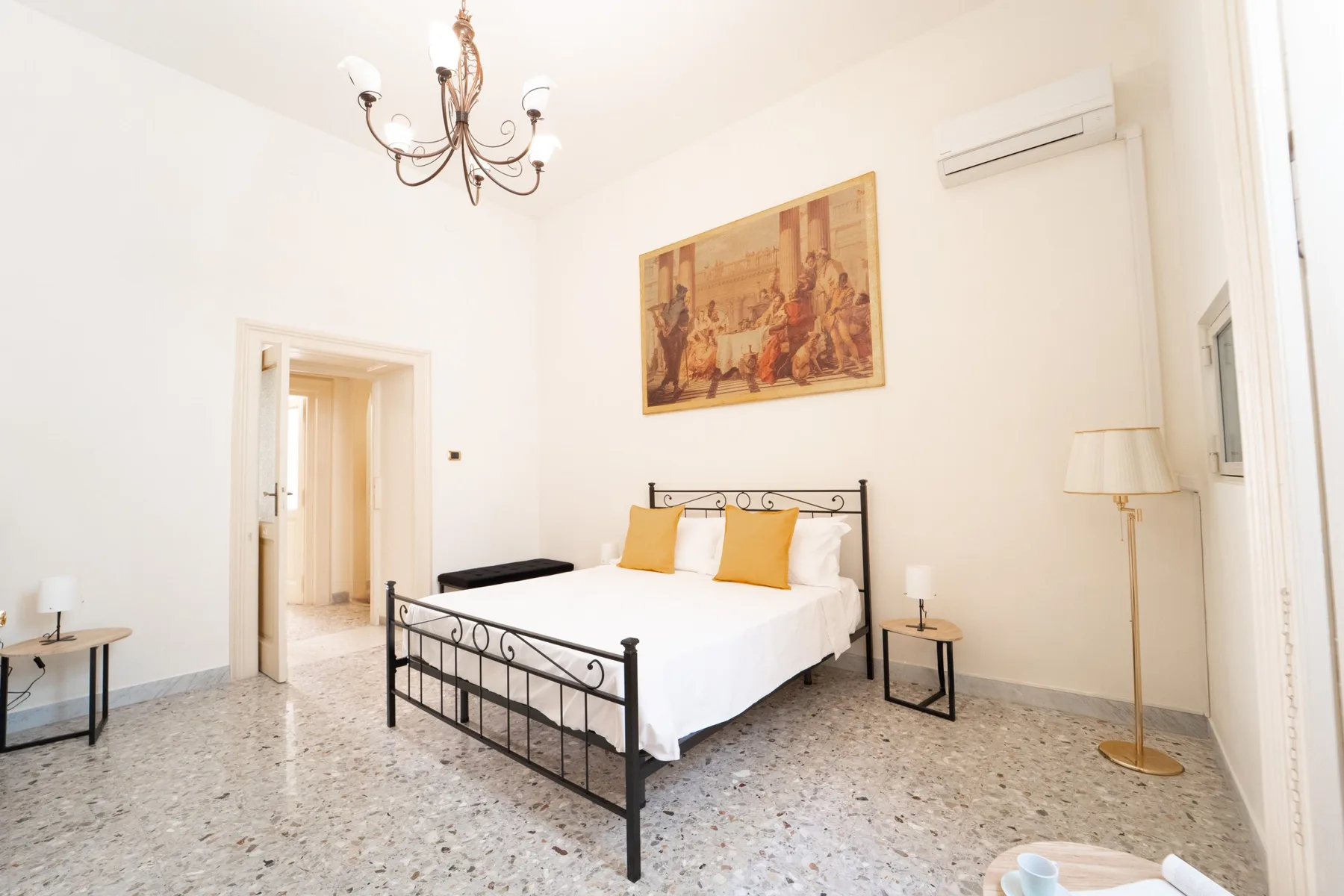 A bright bedroom with a bed, framed artwork, and a chandelier.