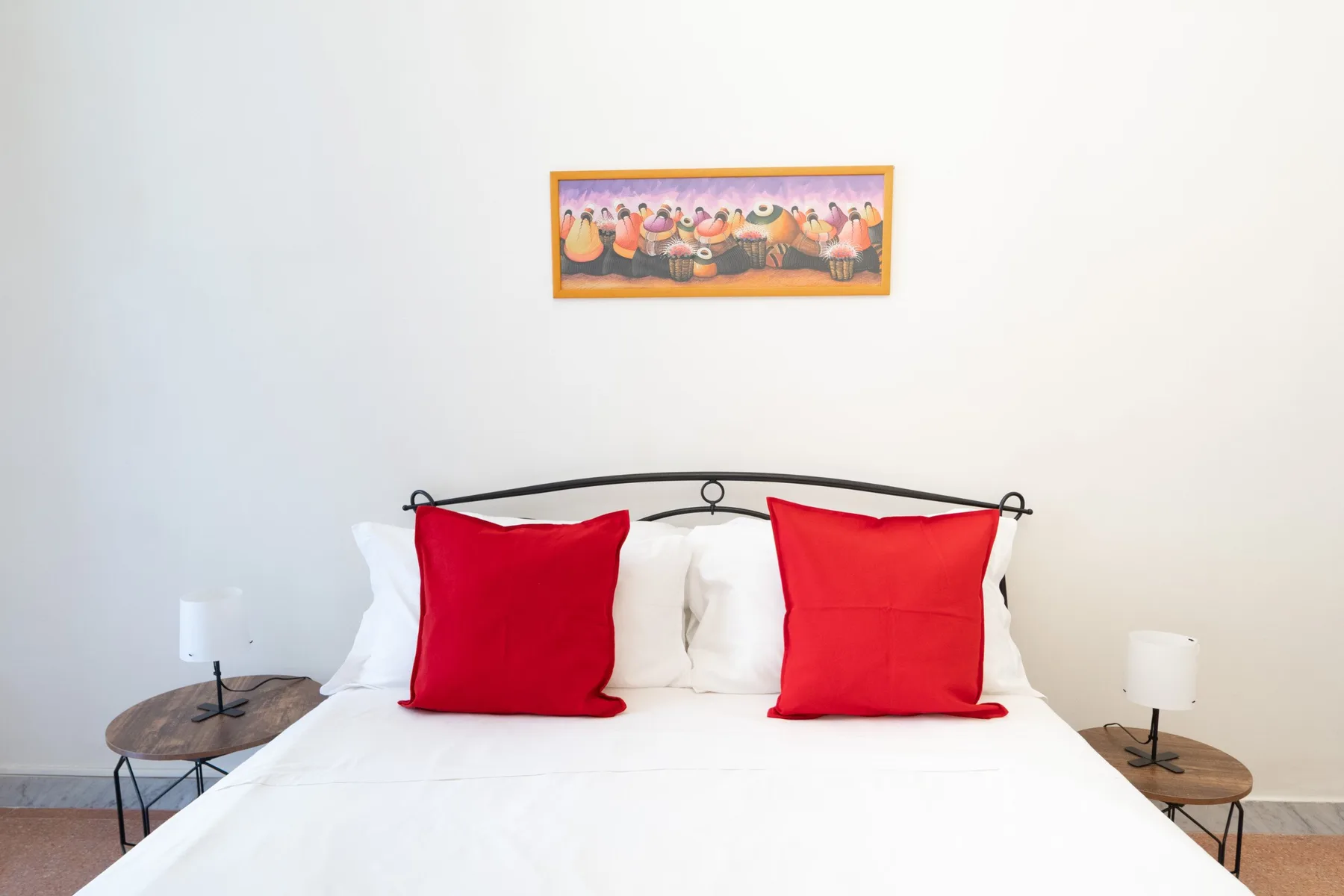 A bedroom with a white bed, red pillows, and framed artwork above the headboard.