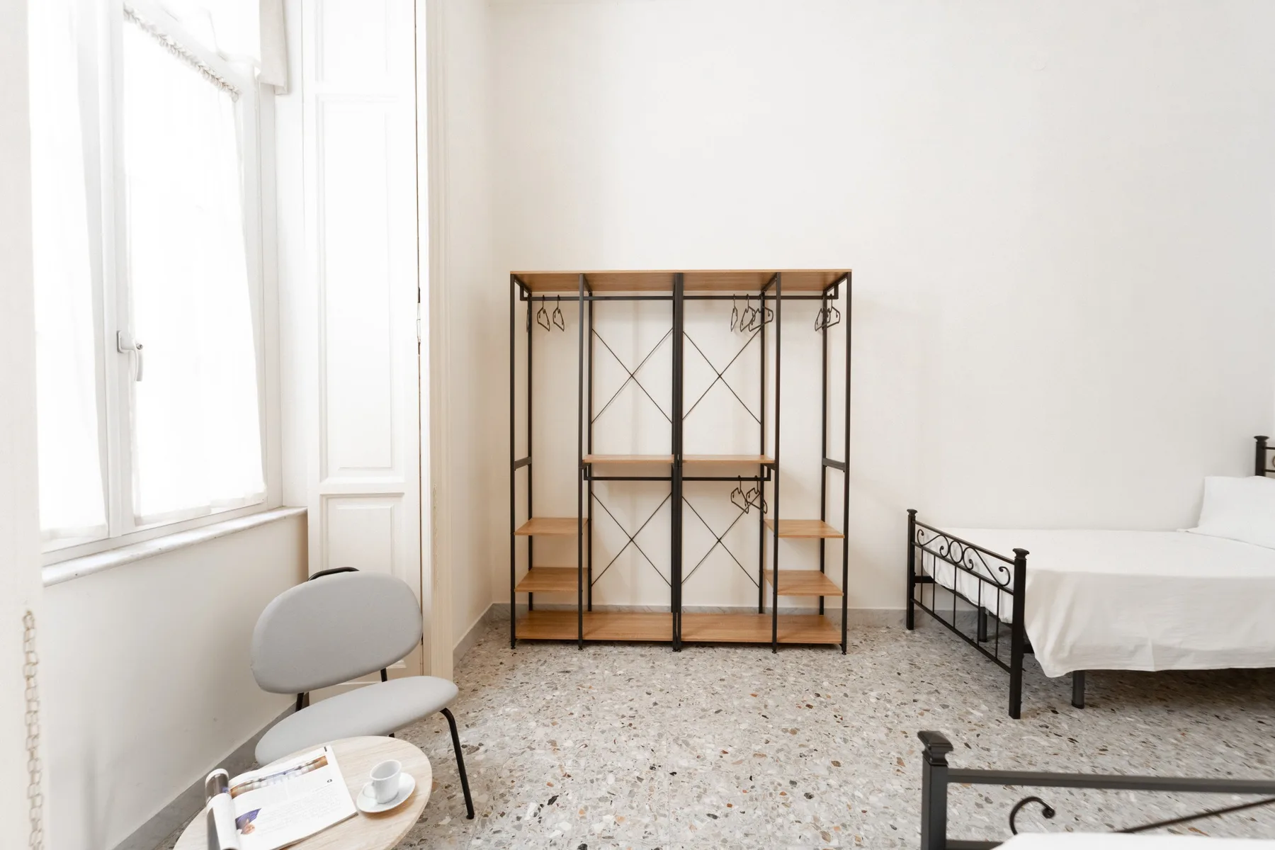 A bright bedroom with a metal bed and open shelving.