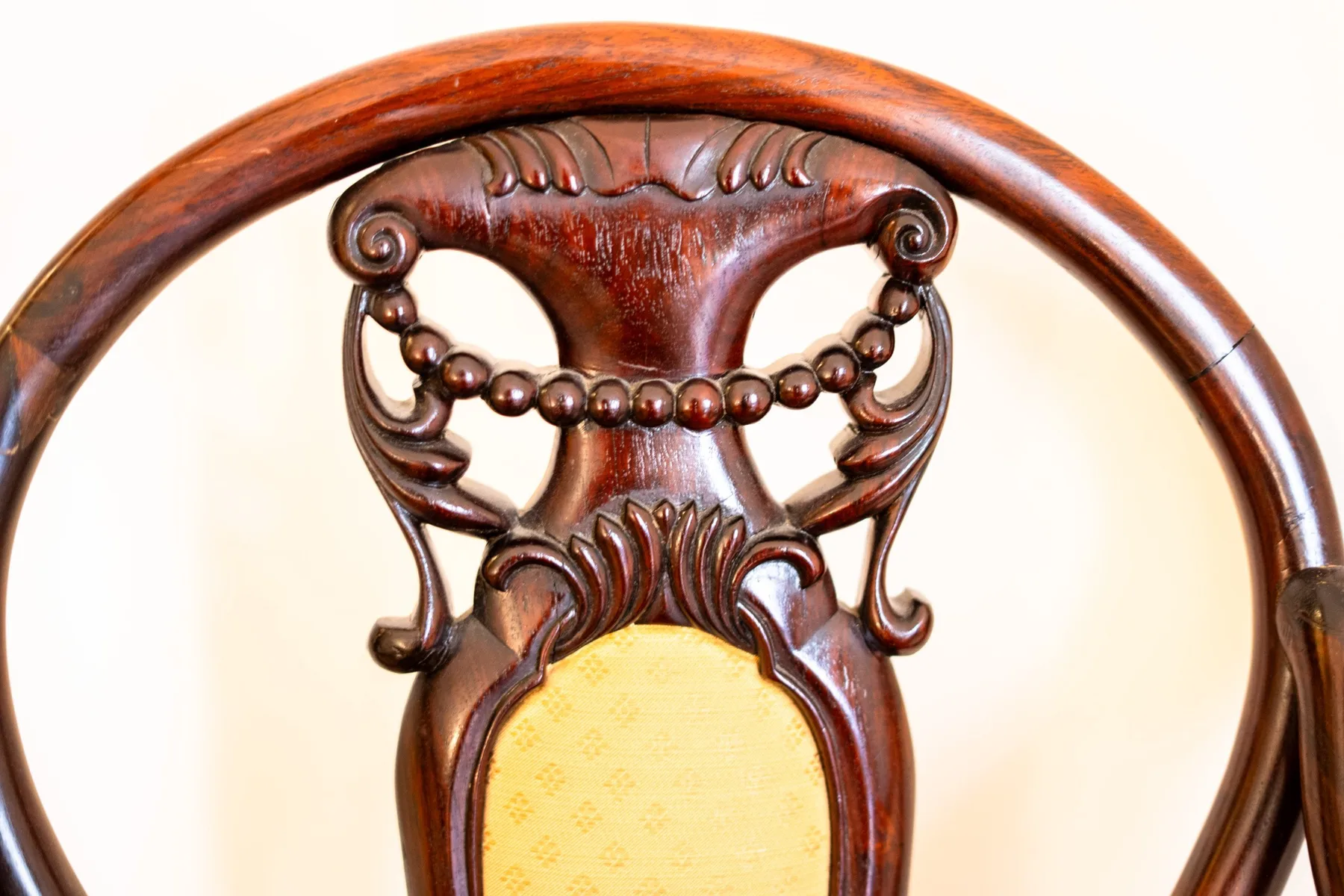 Close-up of an ornate wooden chair with a light upholstered back.