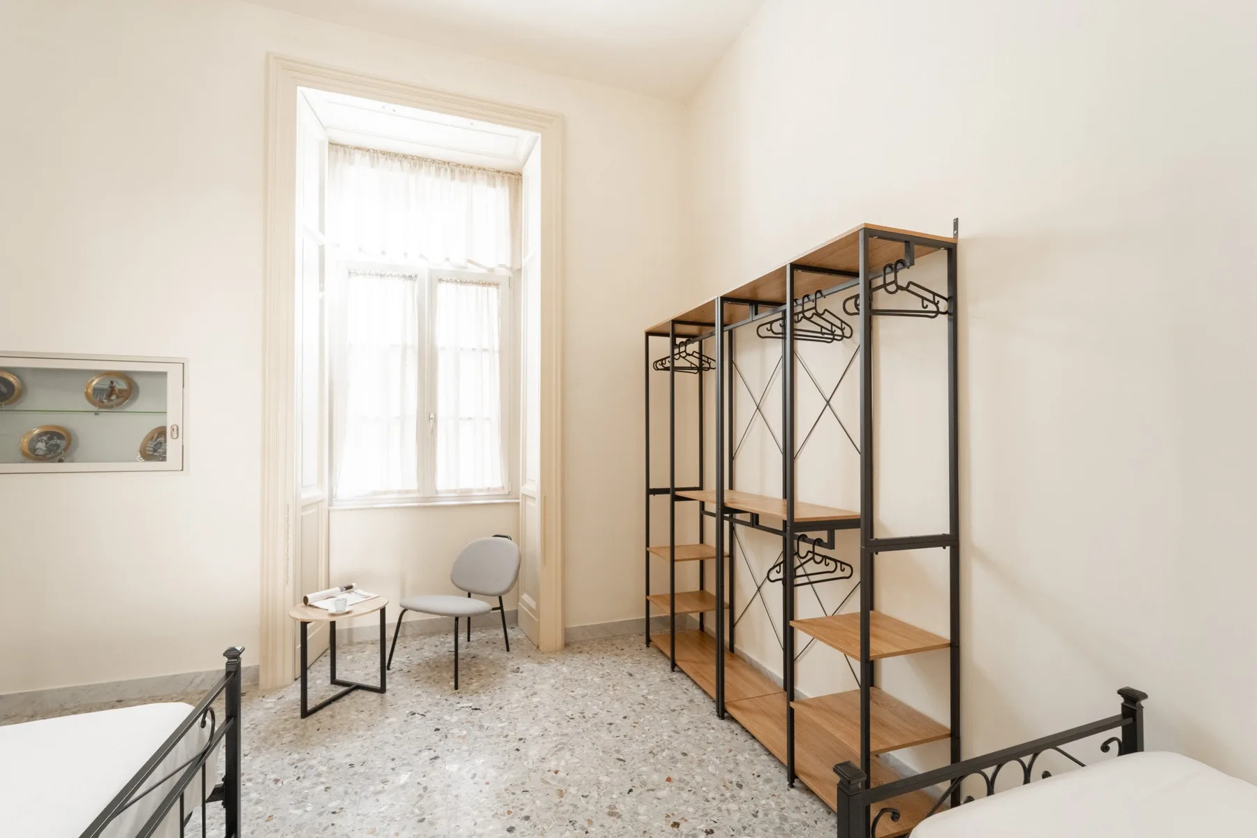 A bright bedroom with black metal bed frames and open clothing racks.