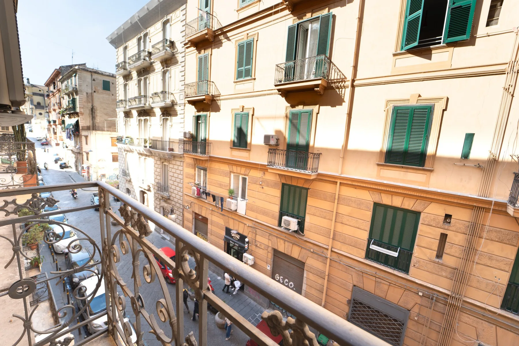 A balcony overlooks a narrow street lined with apartment buildings.
