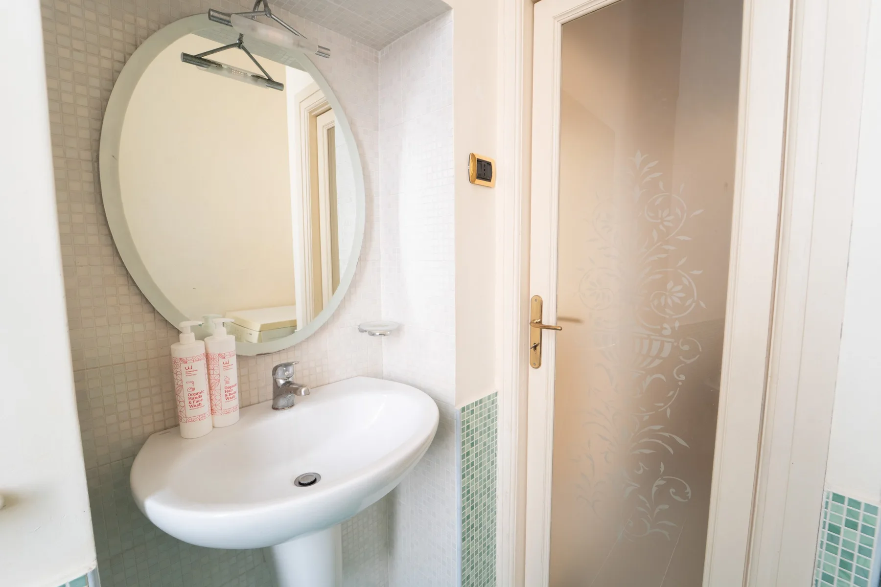 A bathroom sink and oval mirror sit beside a frosted glass door.