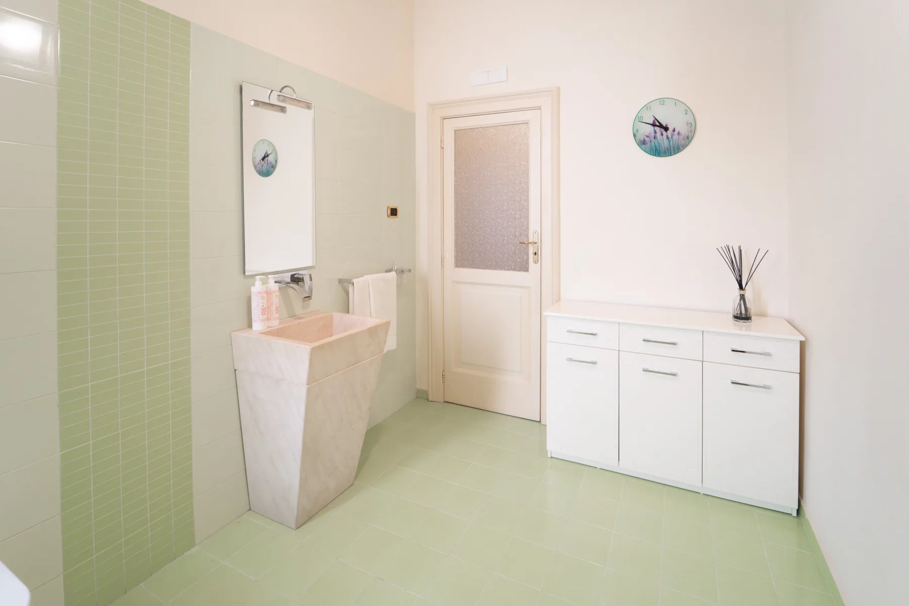 A bright bathroom with a sink, a cabinet, and a frosted-glass door.