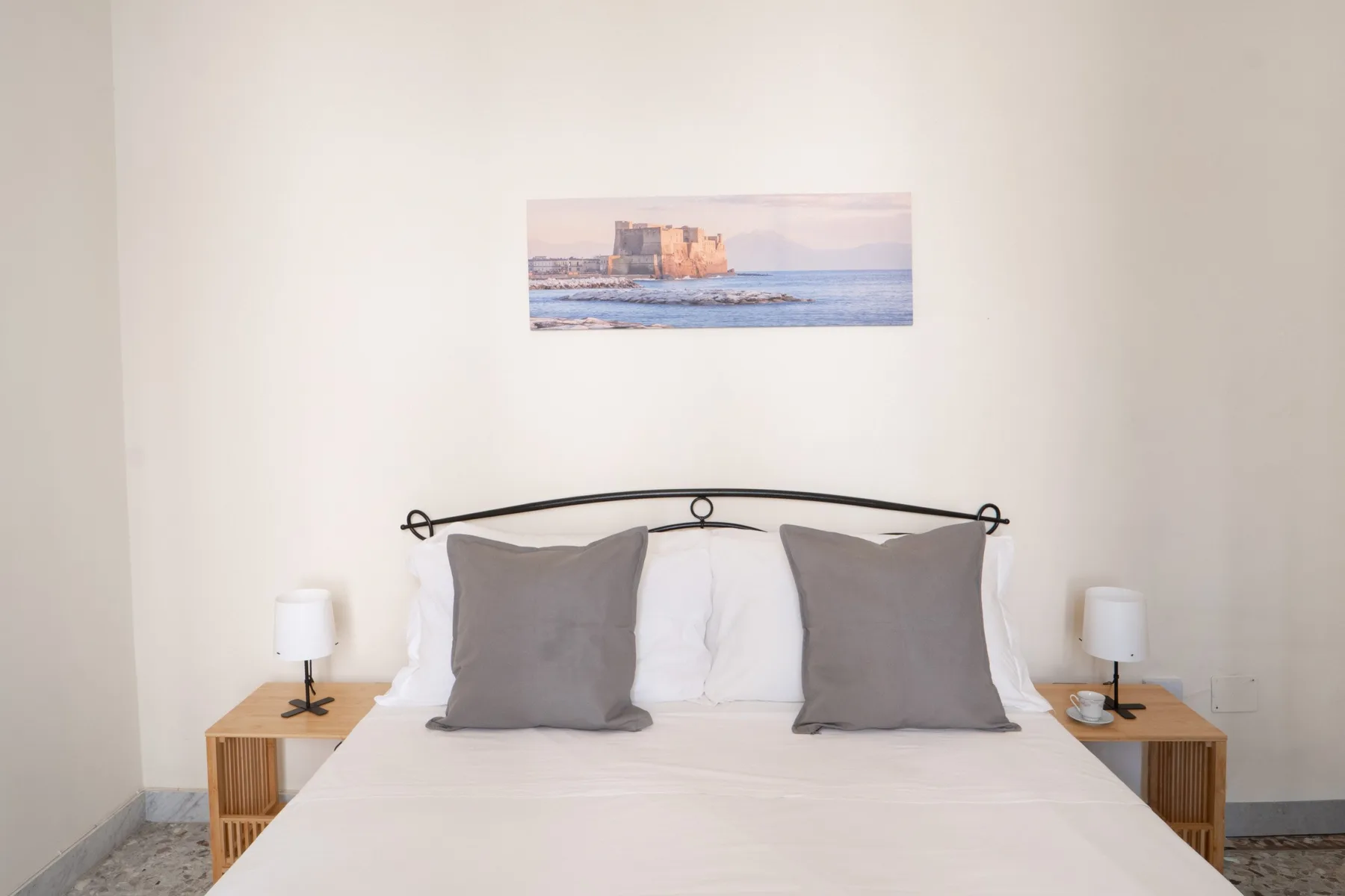 A bedroom with a neatly made bed and a framed coastal picture above it.