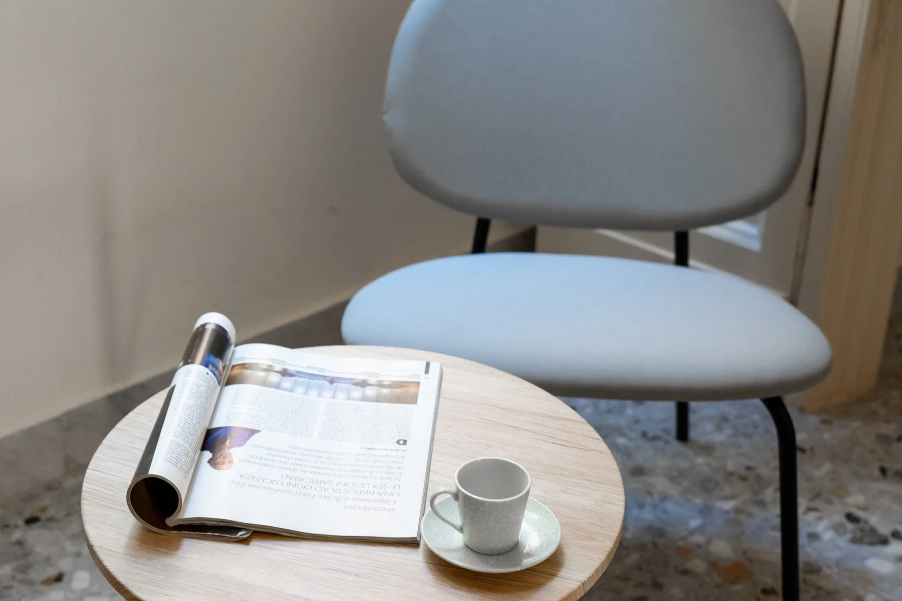 A small seating area with a chair, an open magazine, and a cup on a table.
