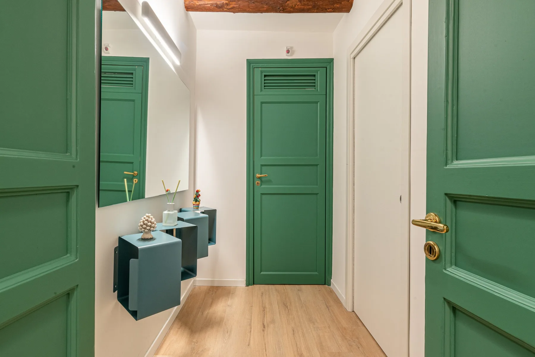 Un pasillo estrecho con puertas verdes y suelo de aspecto madera.