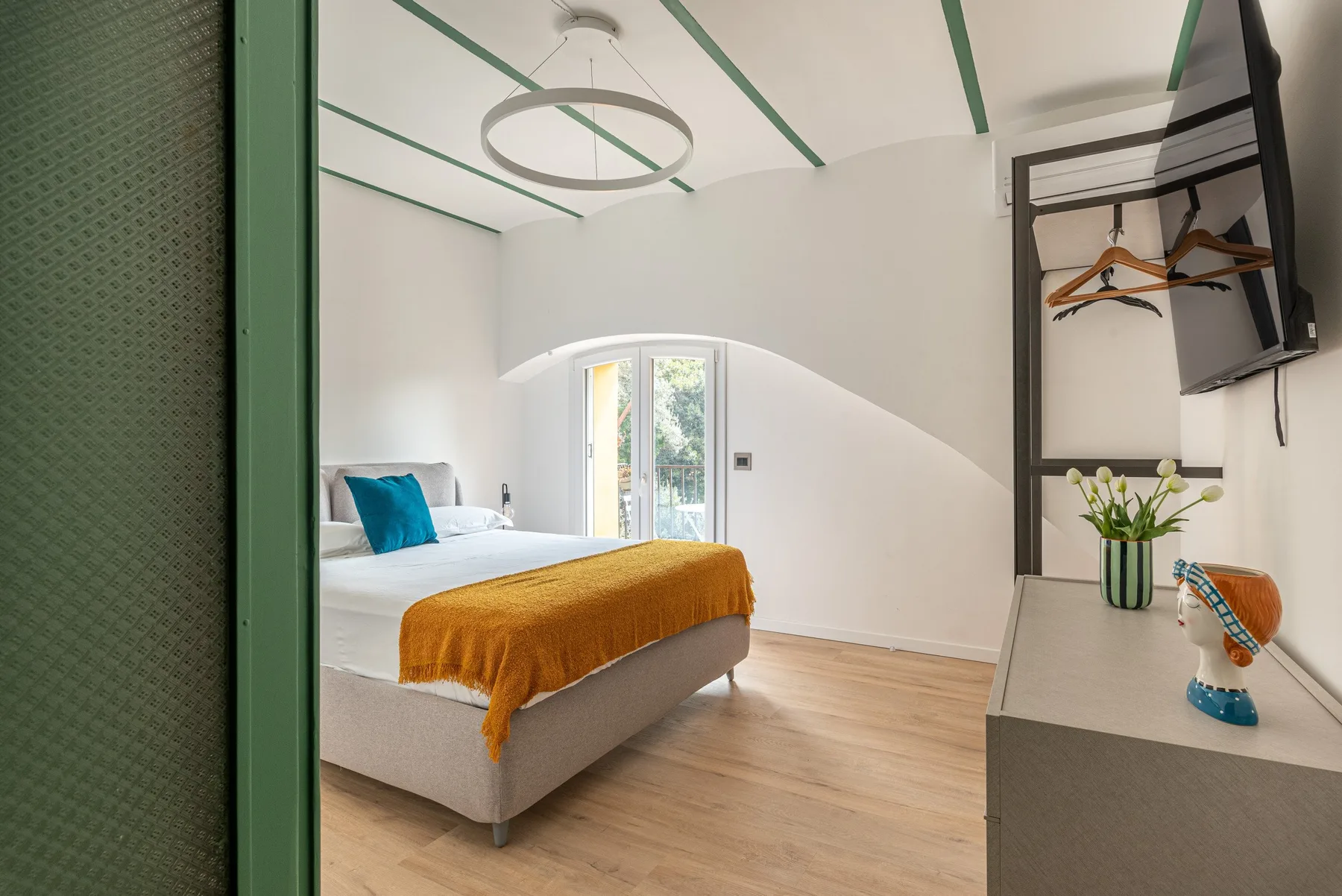 Un dormitorio luminoso con una cama, un cojín turquesa y una zona de armario.