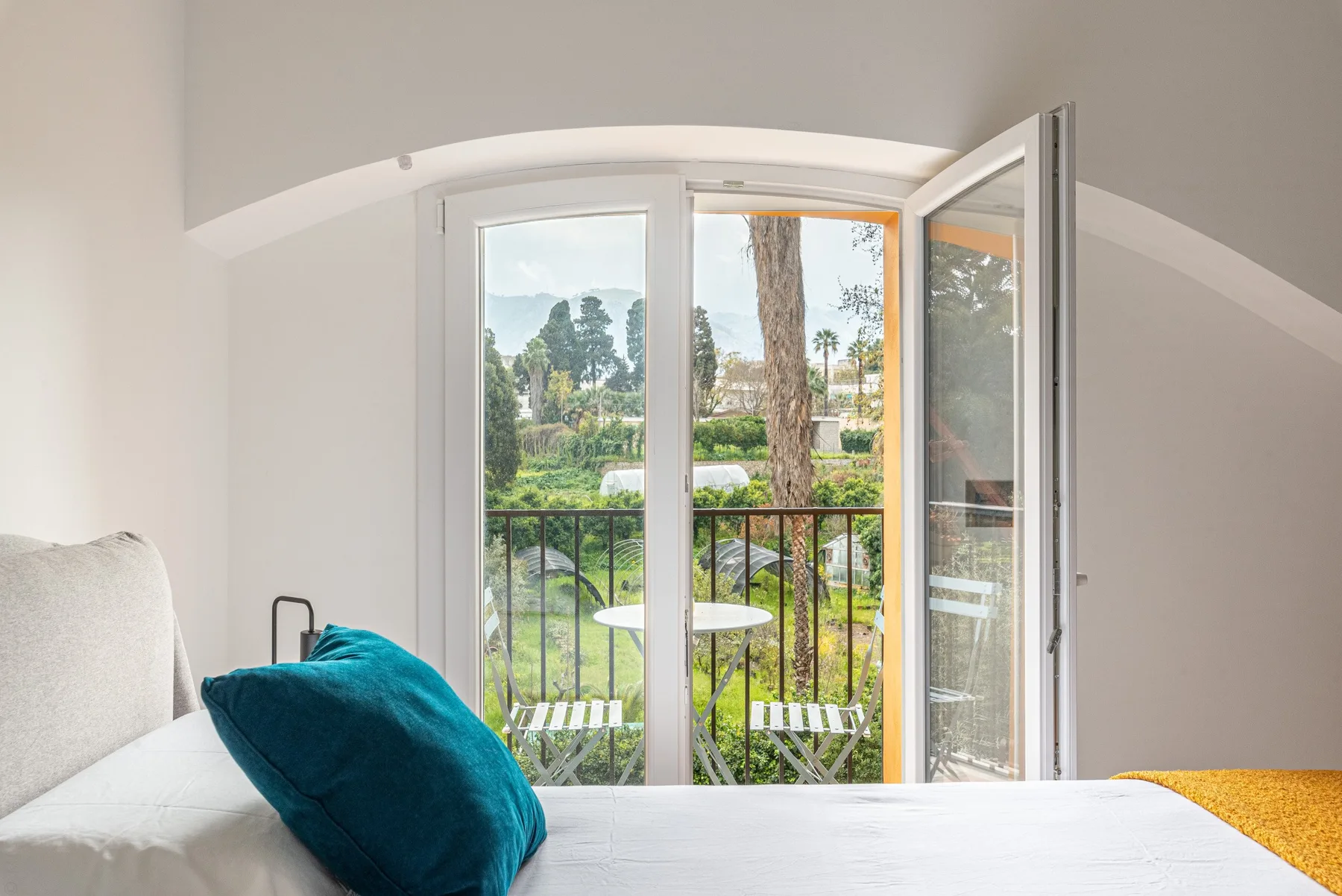 Un dormitorio luminoso se abre a un balcón por una puerta de vidrio, con vegetación al fondo.