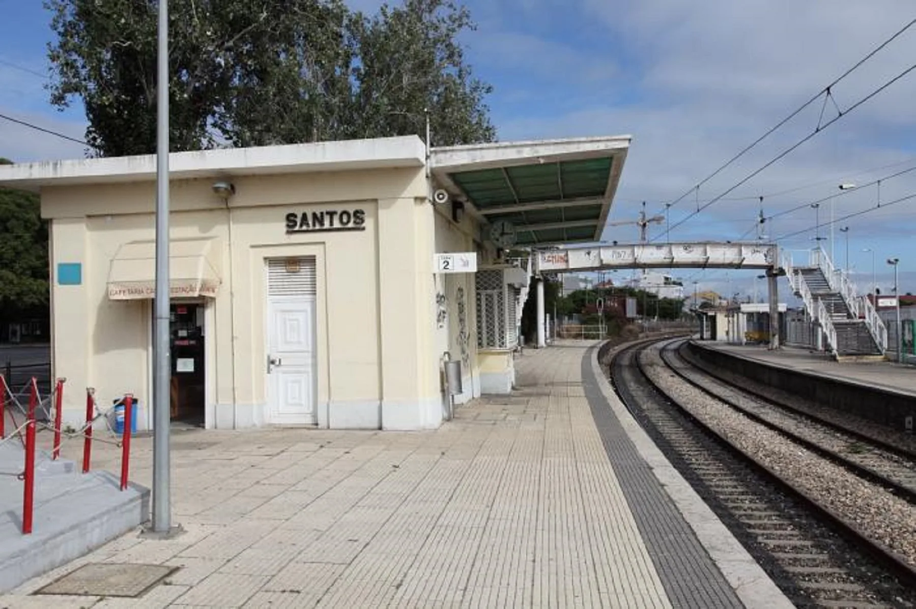 Un andén de estación de tren con vías, un pasillo cubierto y cables aéreos.