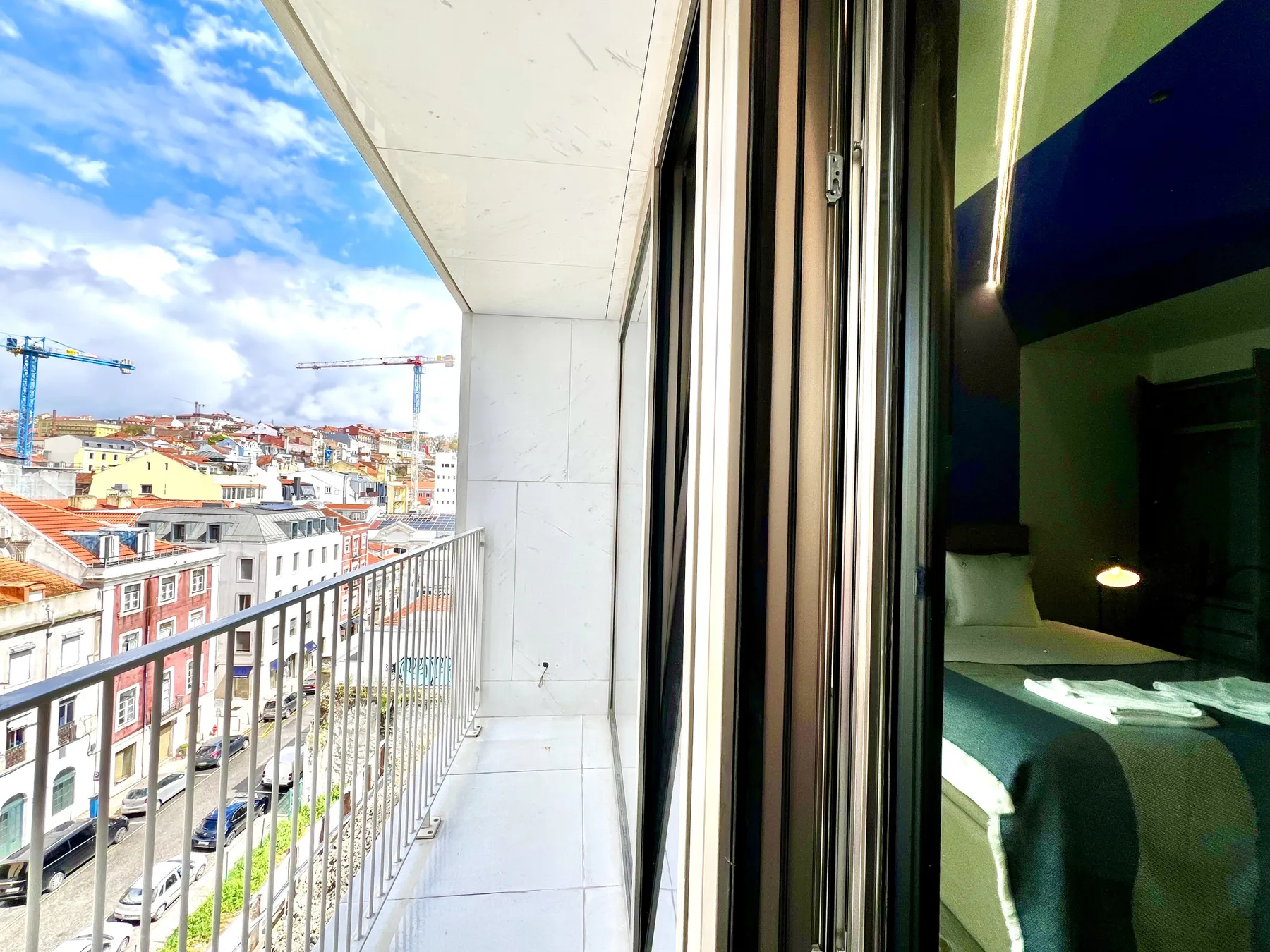 Un balcón estrecho da a los tejados de la ciudad, con un dormitorio visible tras las puertas de cristal abiertas.