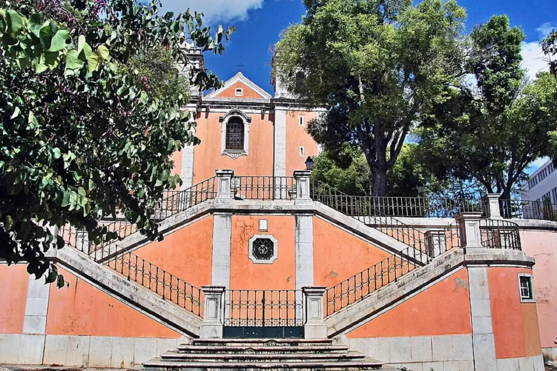 Un edificio naranja se alza detrás de una amplia escalera exterior con barandillas metálicas.
