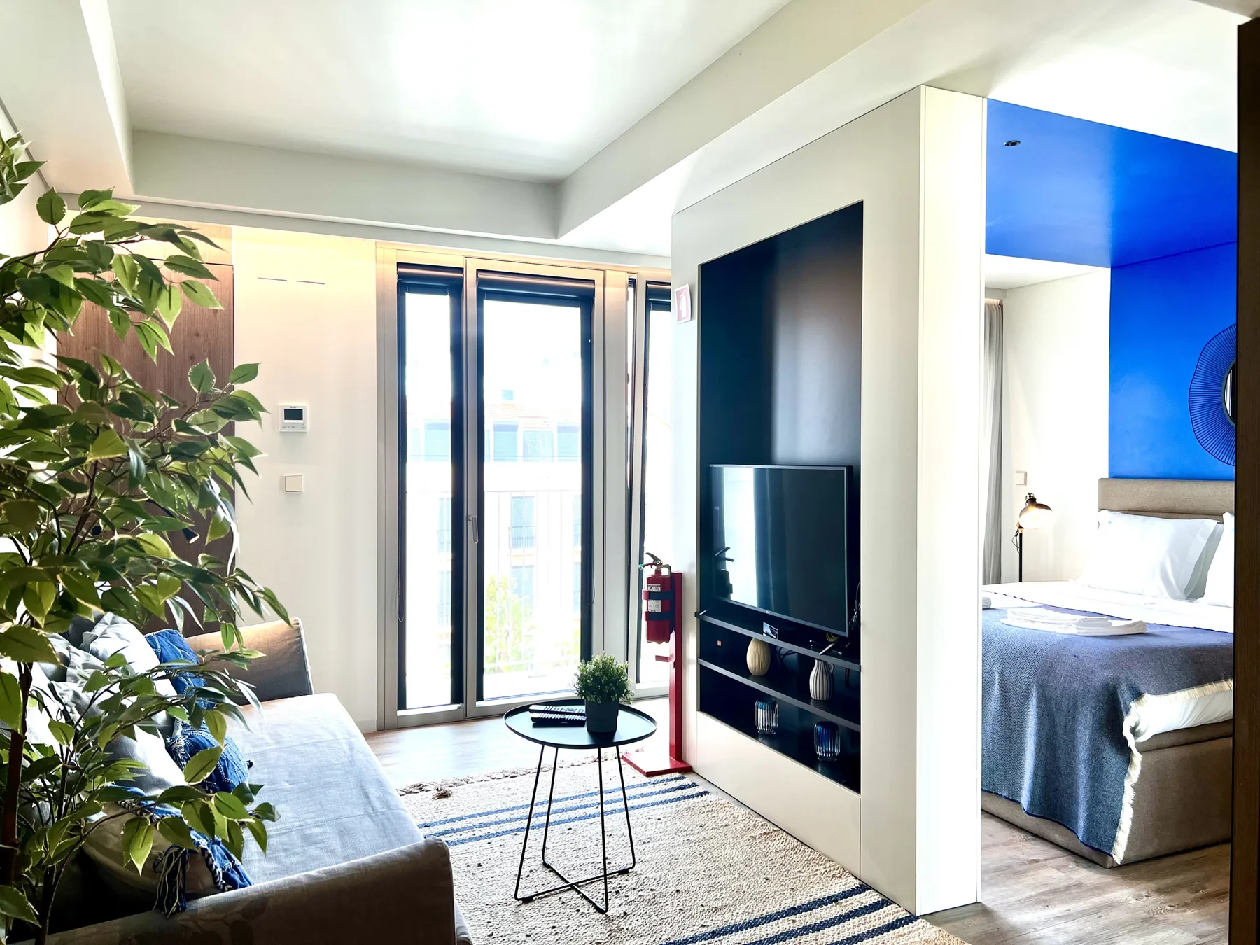 Una sala luminosa con sofá y televisor junto a un dormitorio abierto.