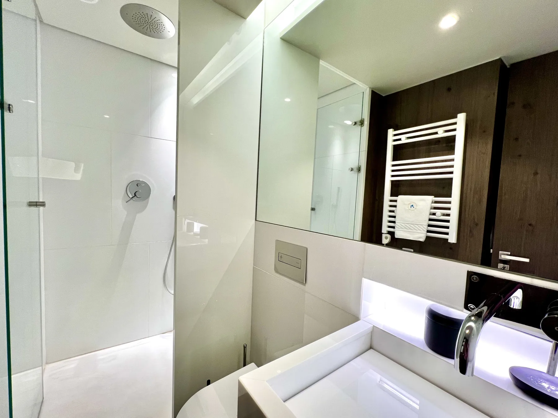 Un baño moderno con ducha de cristal, lavabo y toallero mural.