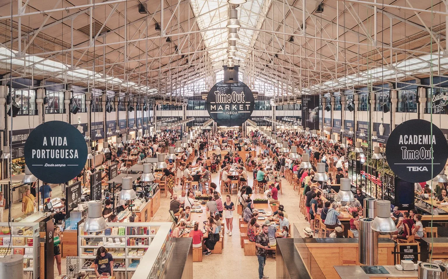 Un mercado cubierto concurrido ocupa un gran salón bajo un techo metálico elevado.