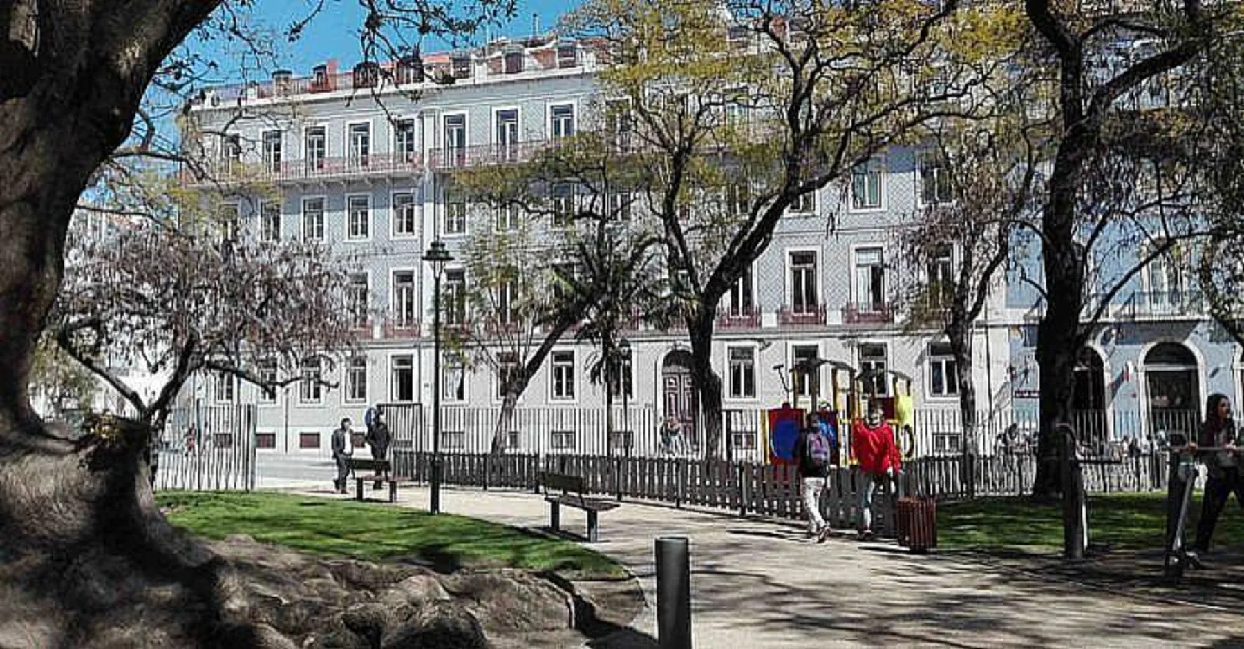 Un sendero arbolado del parque bordea un edificio claro de varias plantas.