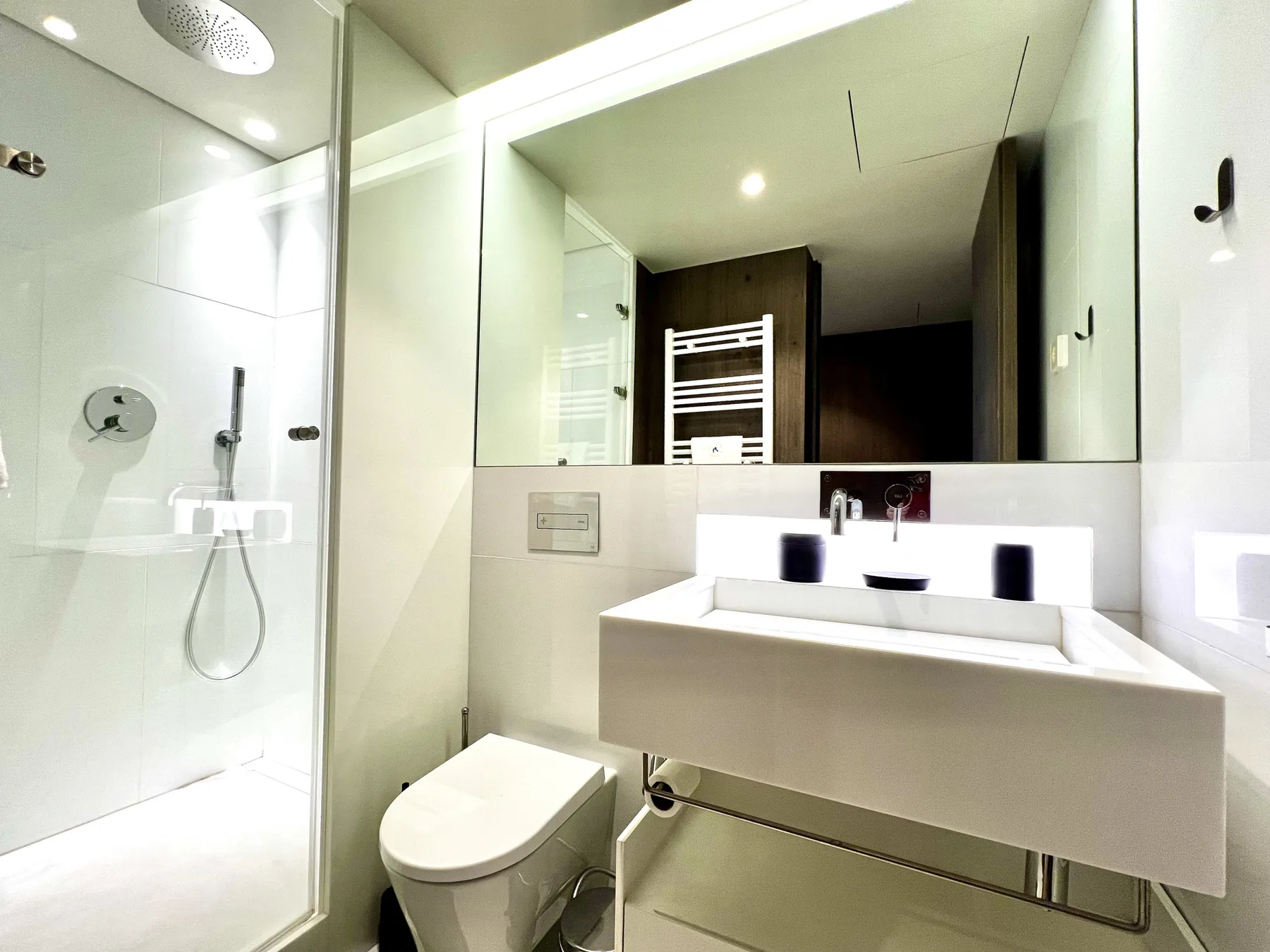 Un baño luminoso con ducha de vidrio, inodoro y un espejo amplio.
