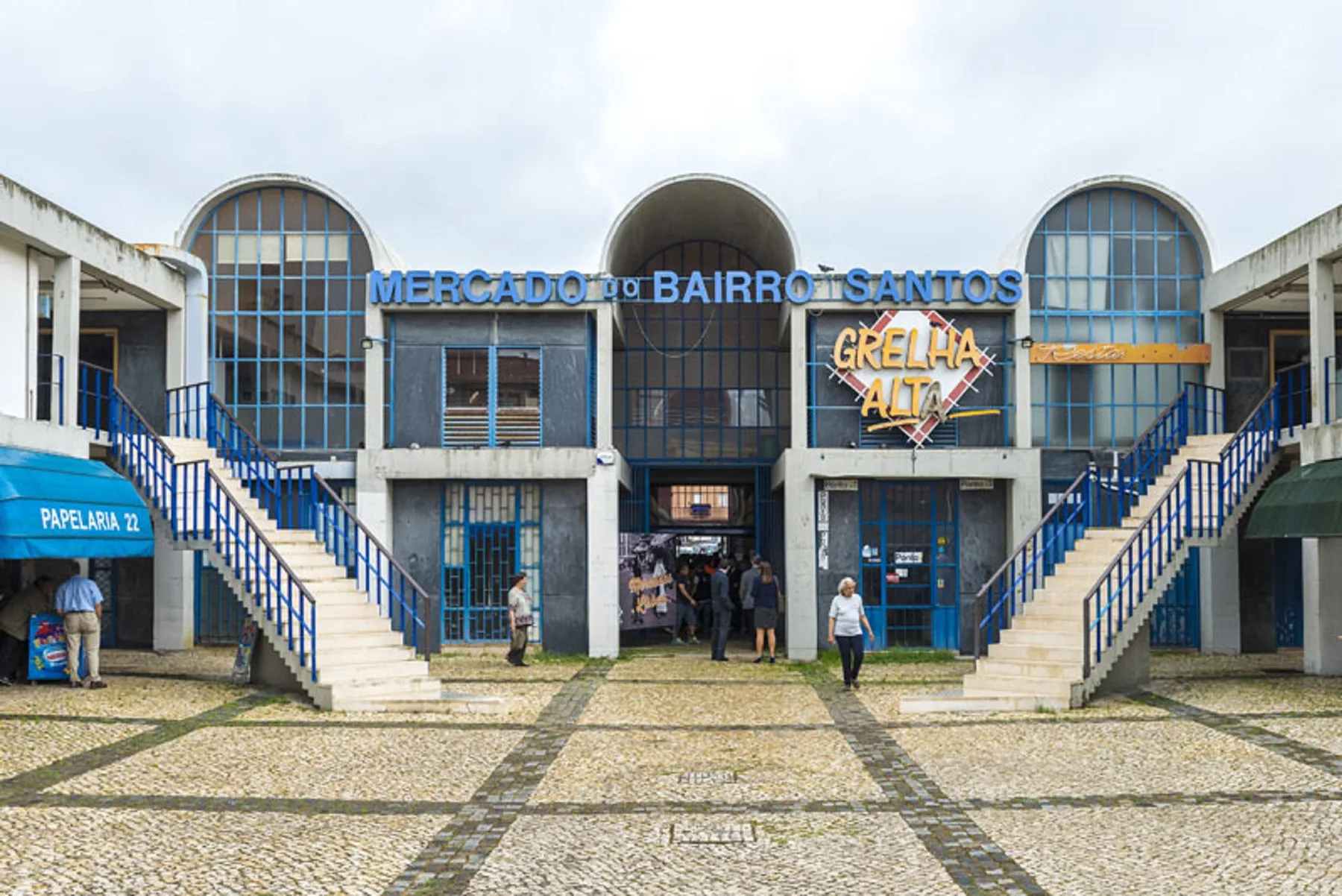 Un mercado con ventanas arqueadas y una amplia explanada pavimentada.