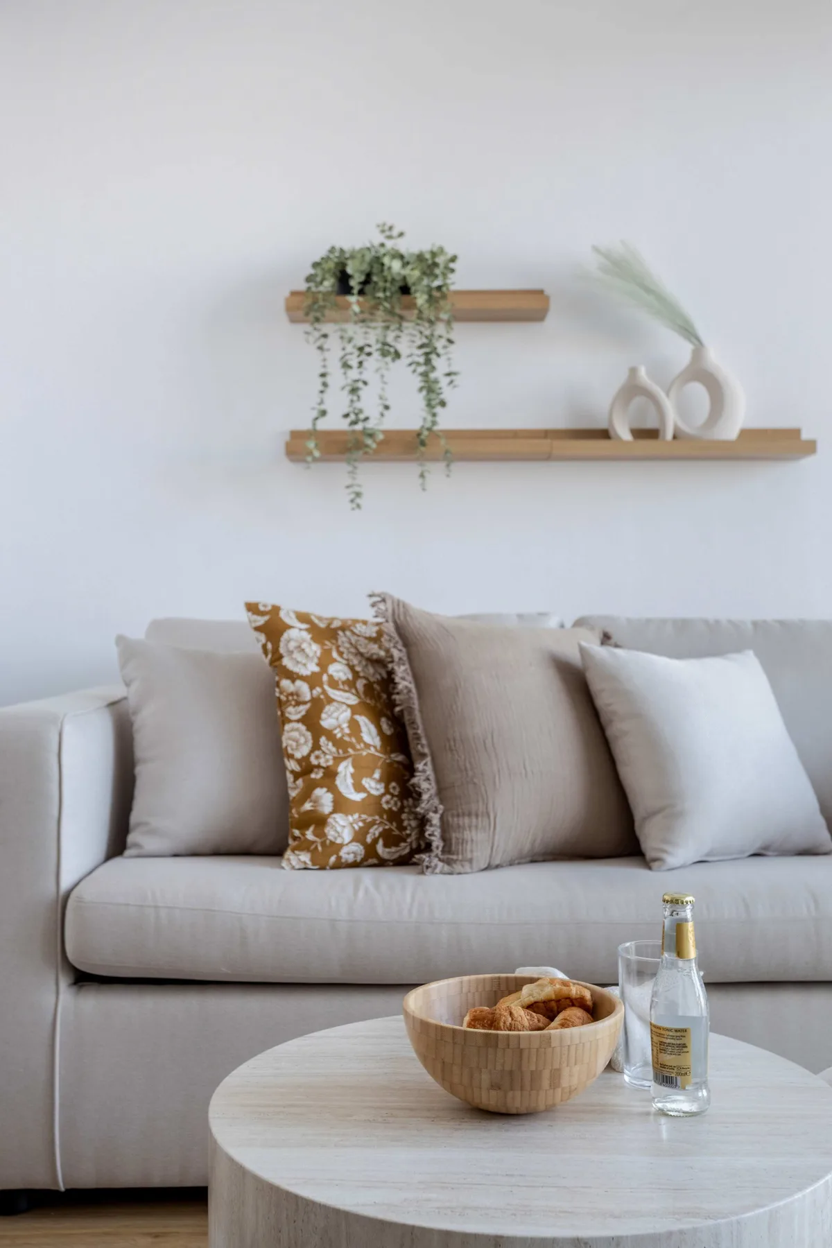 A light-colored sofa sits beneath floating shelves with plants and decorative objects.