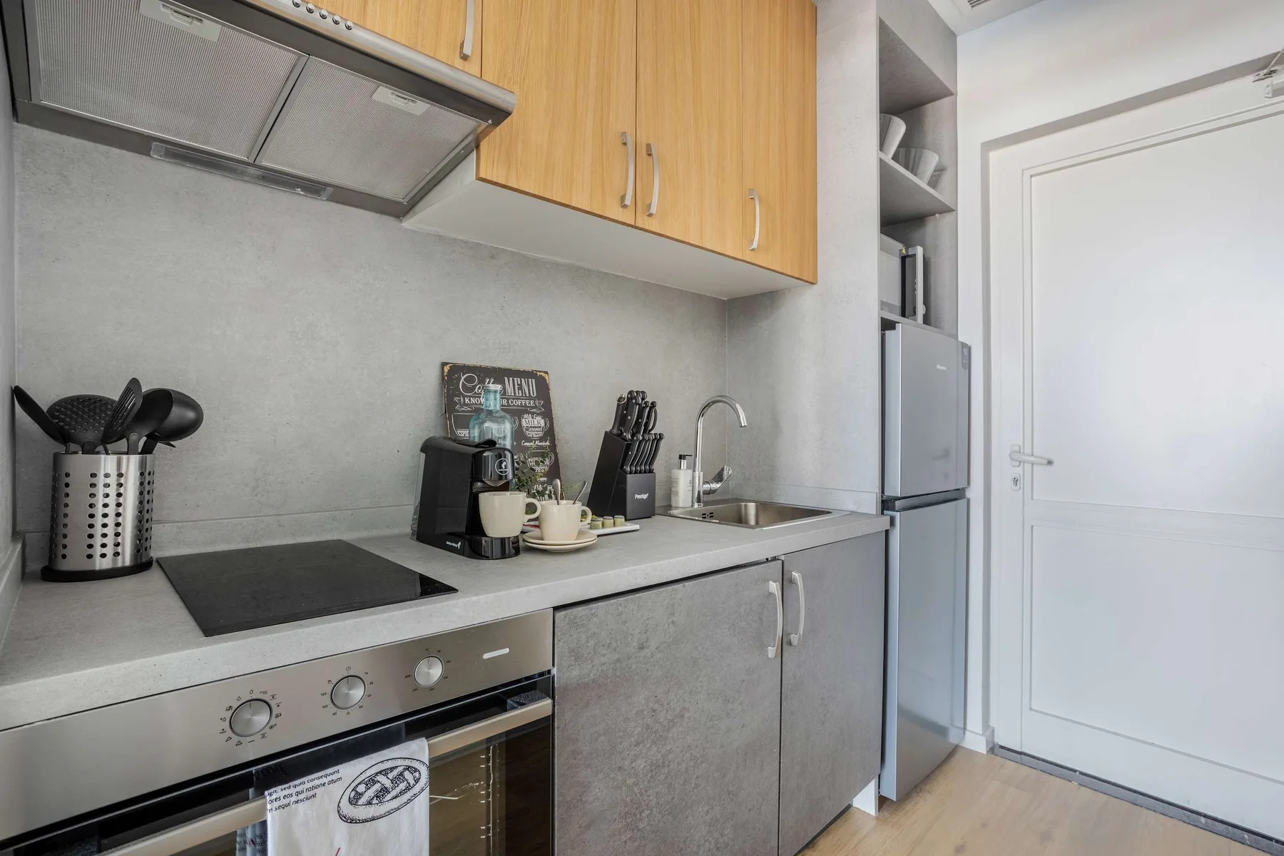 A compact kitchen with a countertop, cooking utensils, and a refrigerator.