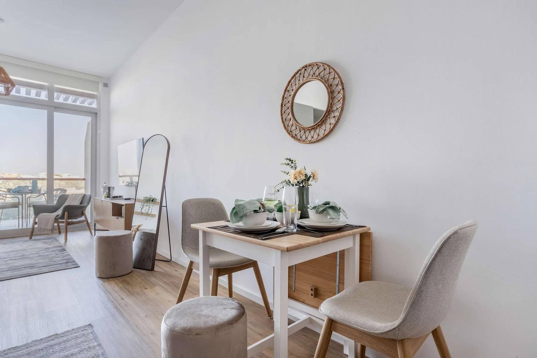 A dining area with a set table and a round mirror on the wall.