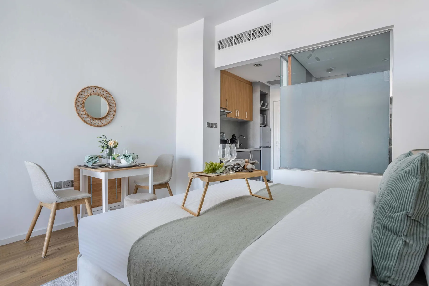 A bright bedroom with a dining table and an adjoining kitchen.