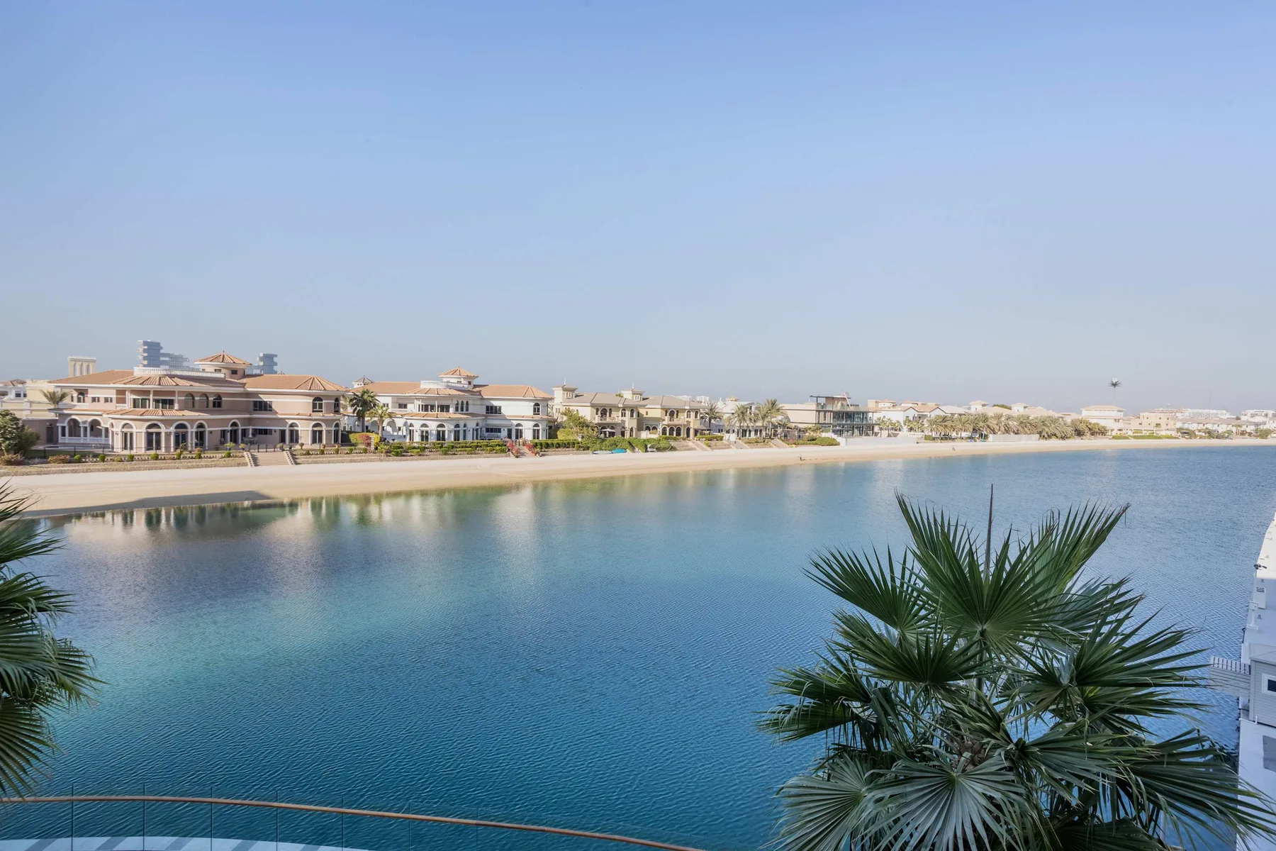 A waterfront view shows calm blue water, palm trees, and buildings along the shore.