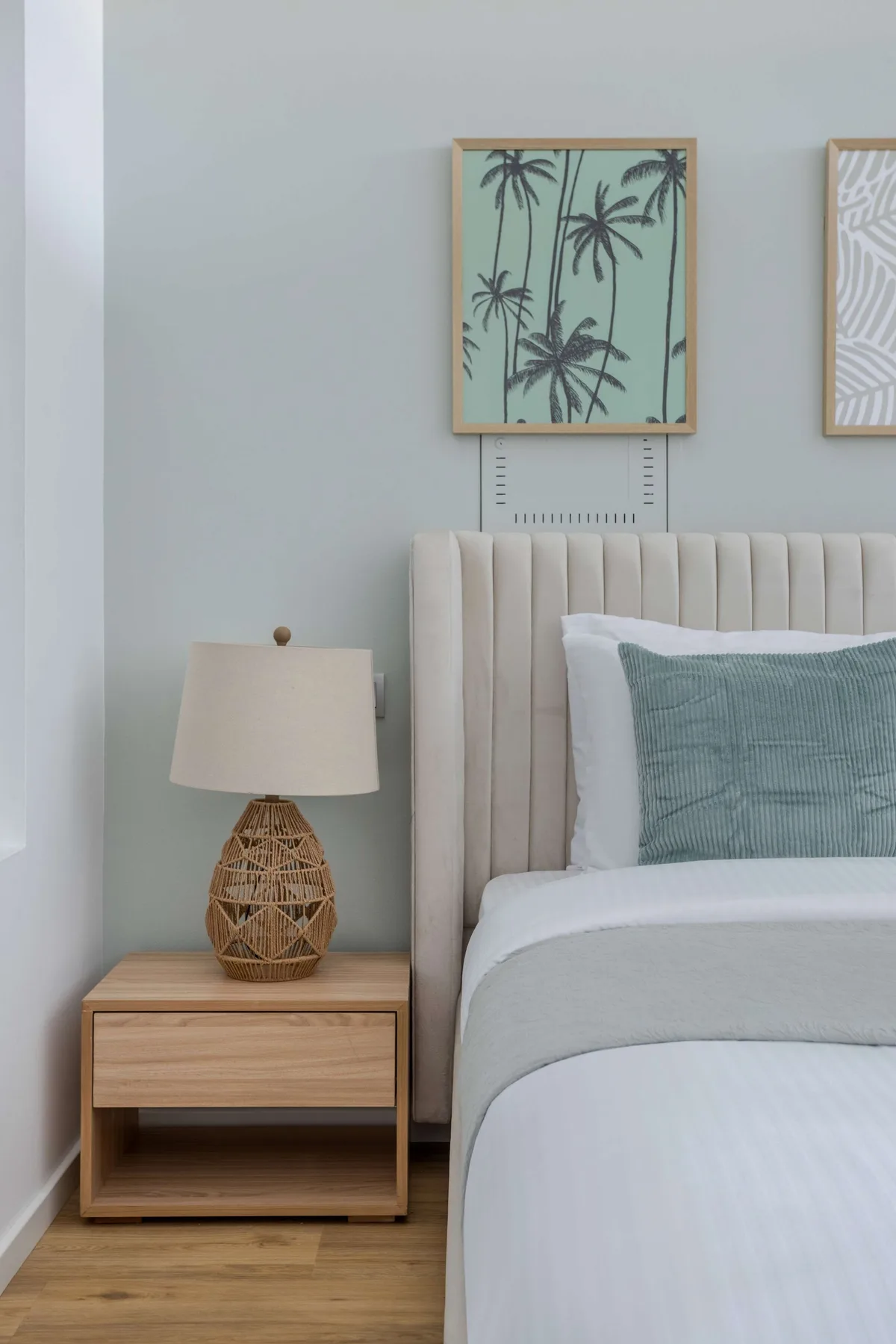 A bedroom with a neatly made bed, a bedside table, and framed wall art.