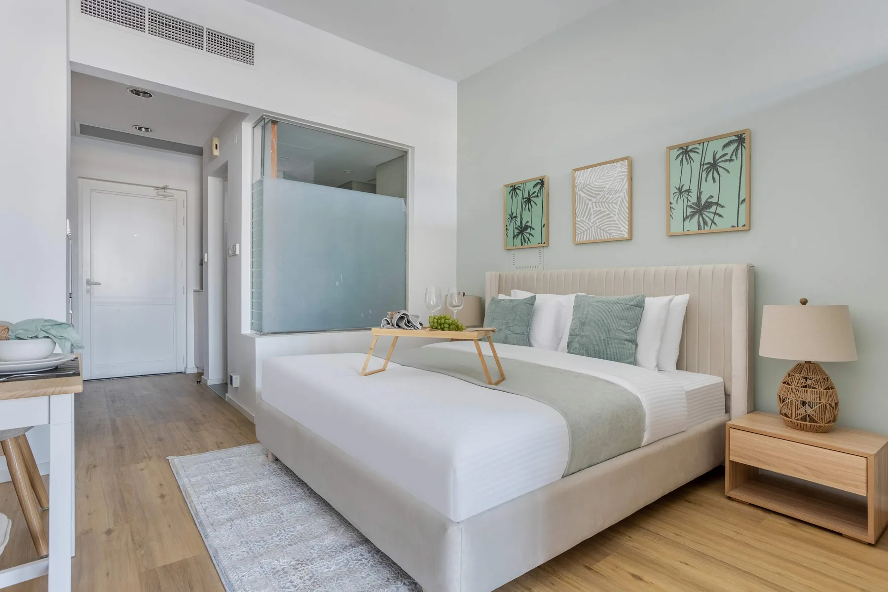 A bright bedroom with a large bed and framed botanical artwork above the headboard.