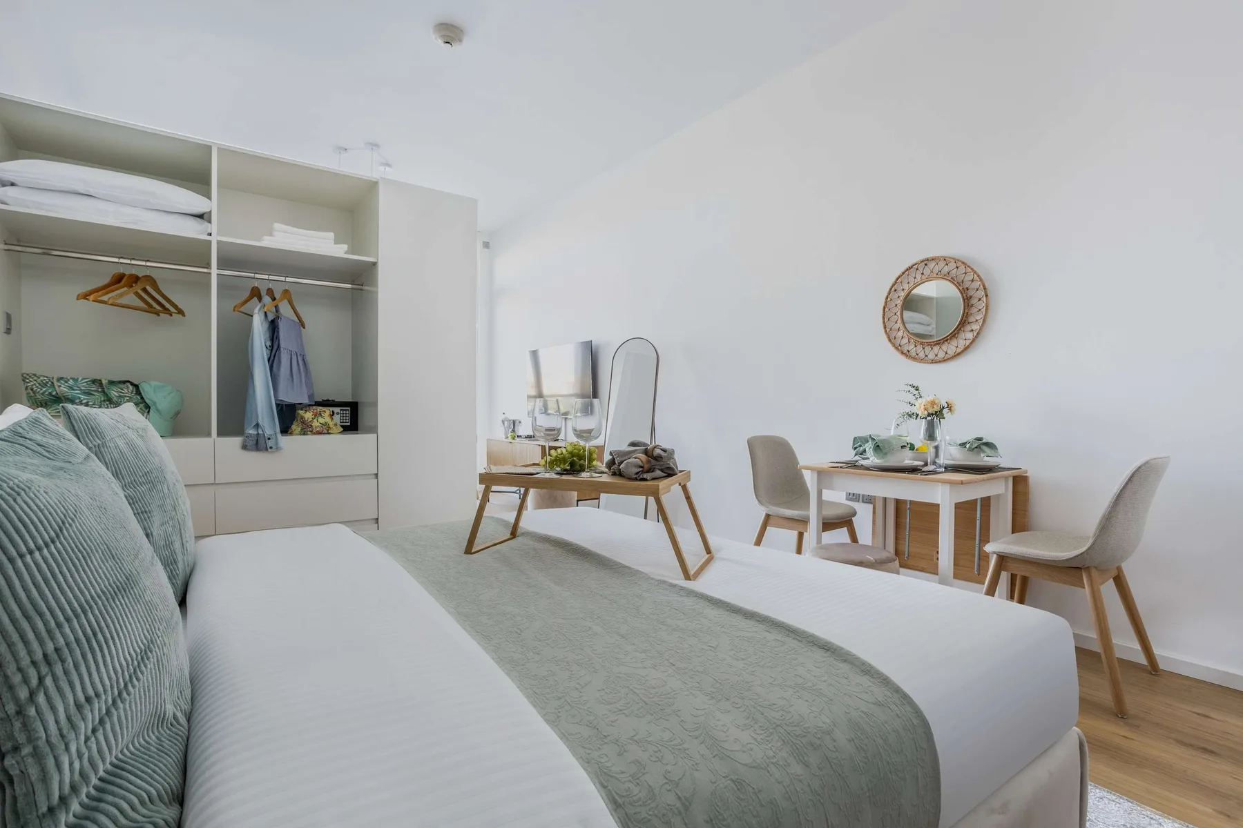 A bright bedroom with an open wardrobe and a small dining table.