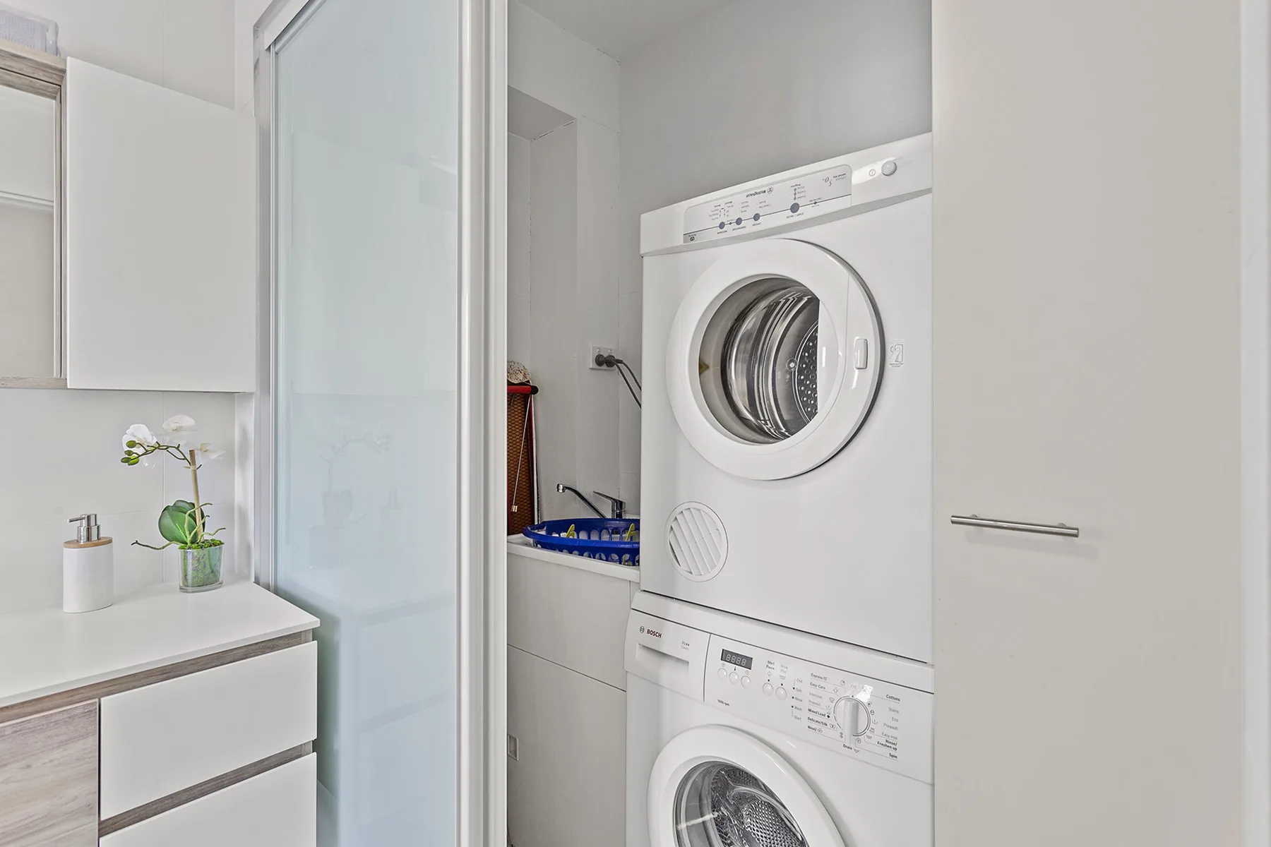 Una zona de lavandería con lavadora y secadora apiladas junto a un tocador de baño.