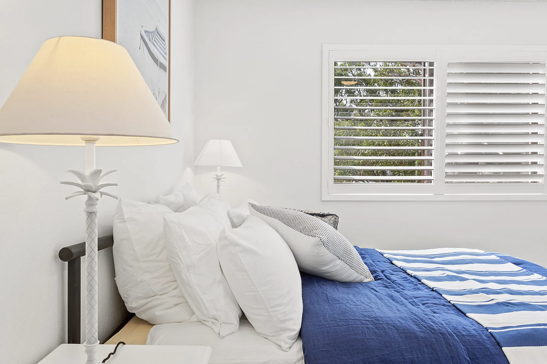 Dormitorio con una cama bien tendida y ropa de cama azul junto a ventanas con persianas.