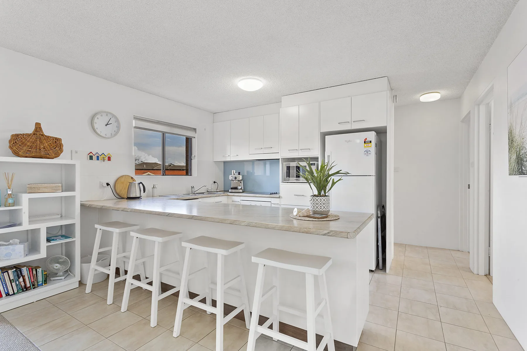 Una cocina luminosa con gabinetes blancos, una encimera larga y asientos de barra.