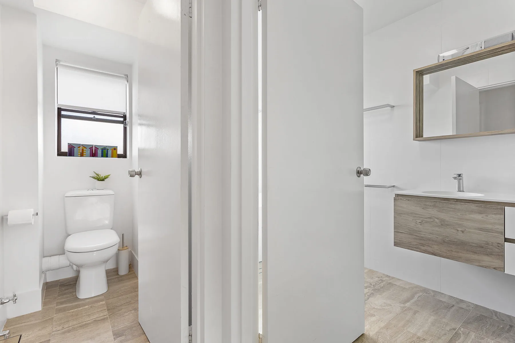 Baño luminoso con inodoro, lavabo y un espejo grande.