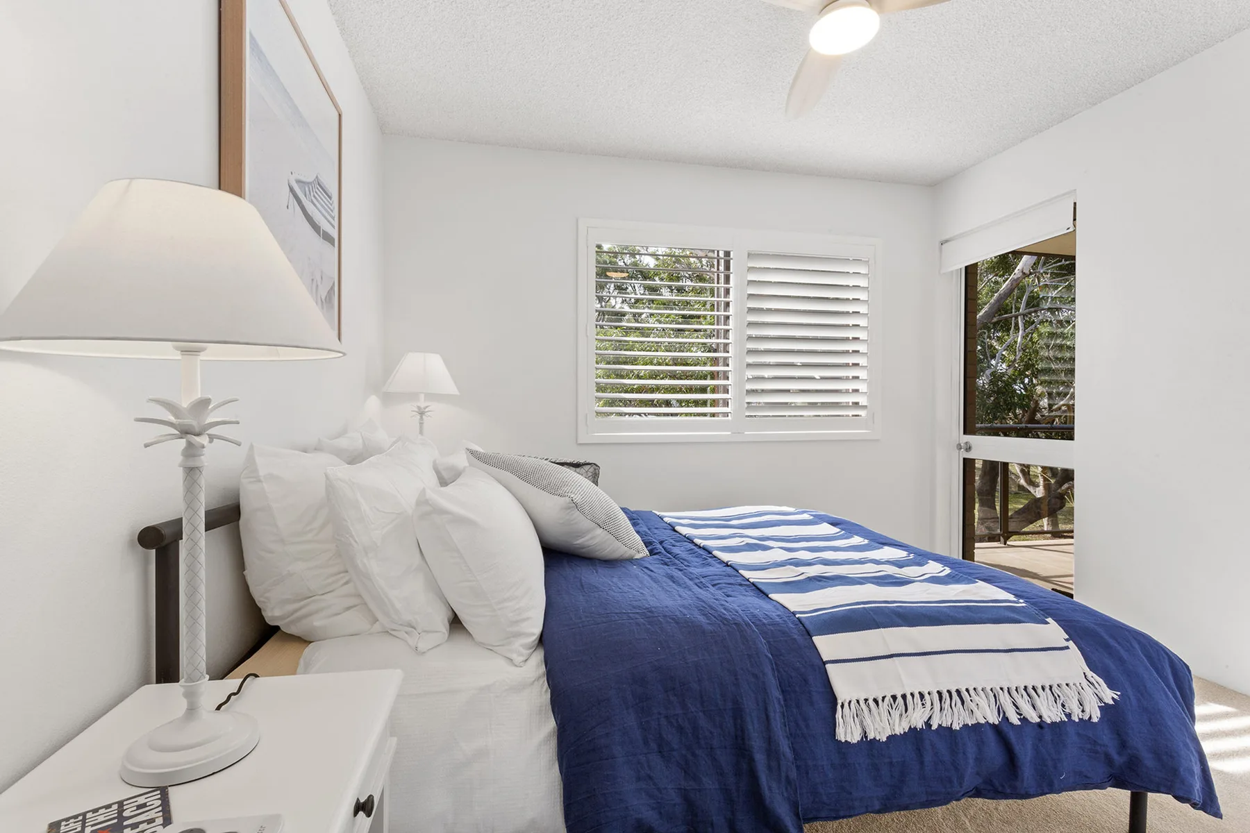 Un dormitorio luminoso con una cama vestida con ropa de cama azul y blanca.