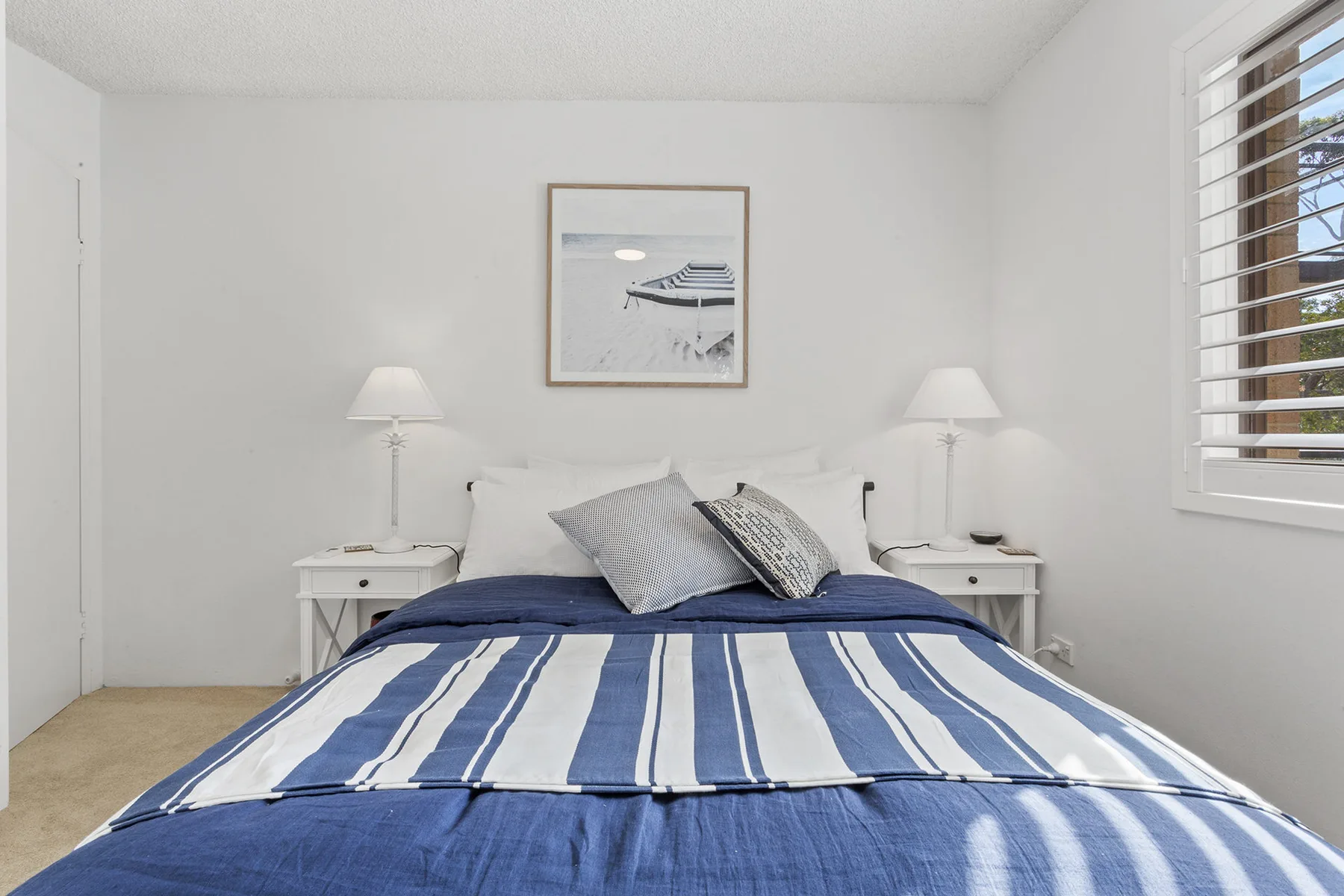 Un dormitorio con una colcha de rayas azules y blancas y un cuadro enmarcado.
