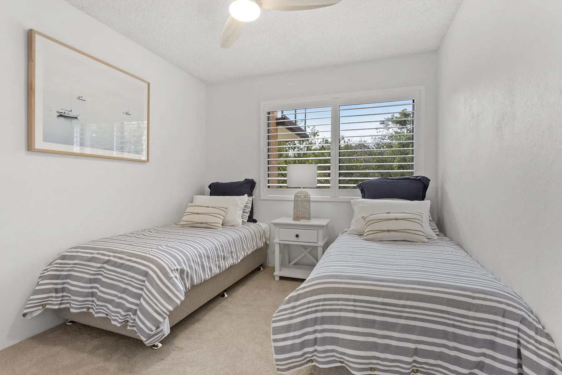 Un dormitorio con dos camas individuales, ropa de cama a rayas y una ventana con persianas.