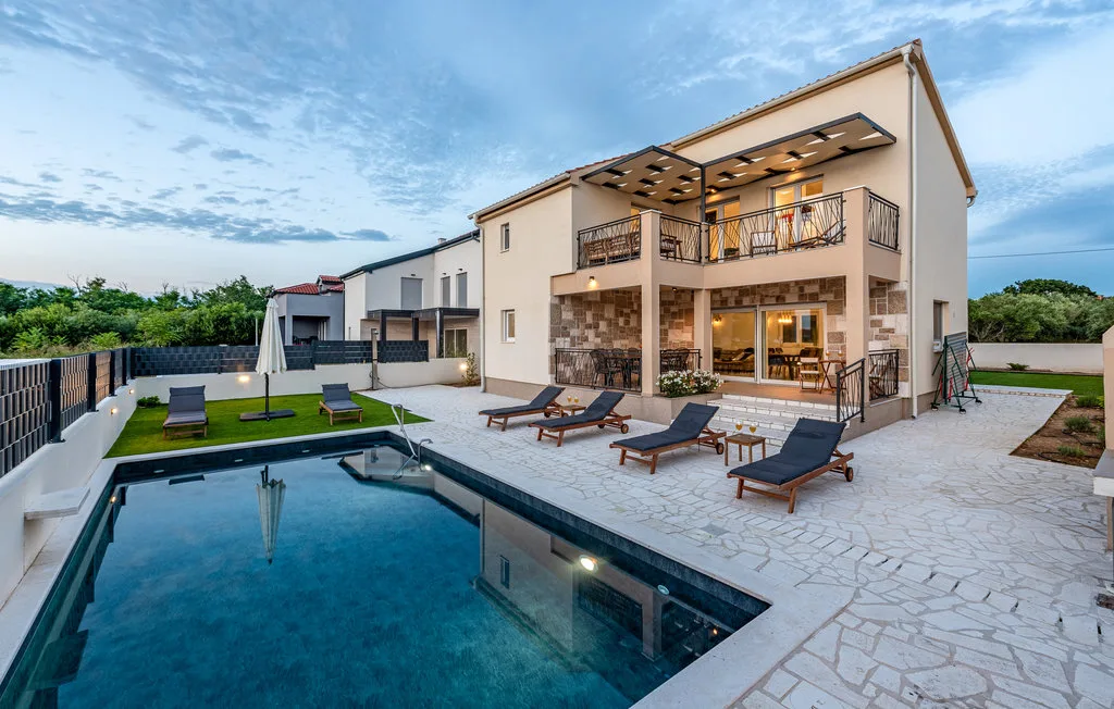 A modern house opens onto a swimming pool and paved patio.