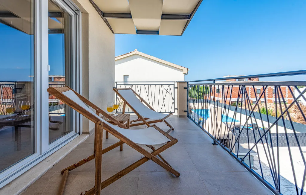 A balcony with reclining seating overlooks a swimming pool and nearby buildings.