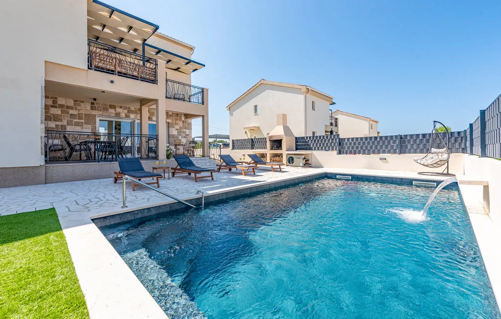 An outdoor swimming pool beside modern buildings, with lounge seating along the water.