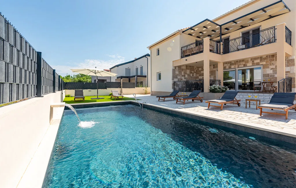 Una piscina junto a una casa moderna, con asientos de descanso en el patio.