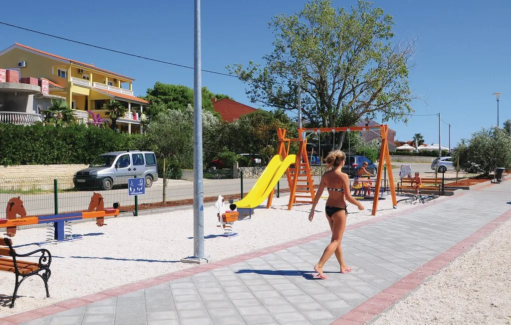 A playground has a yellow slide, swings, and a paved walkway.