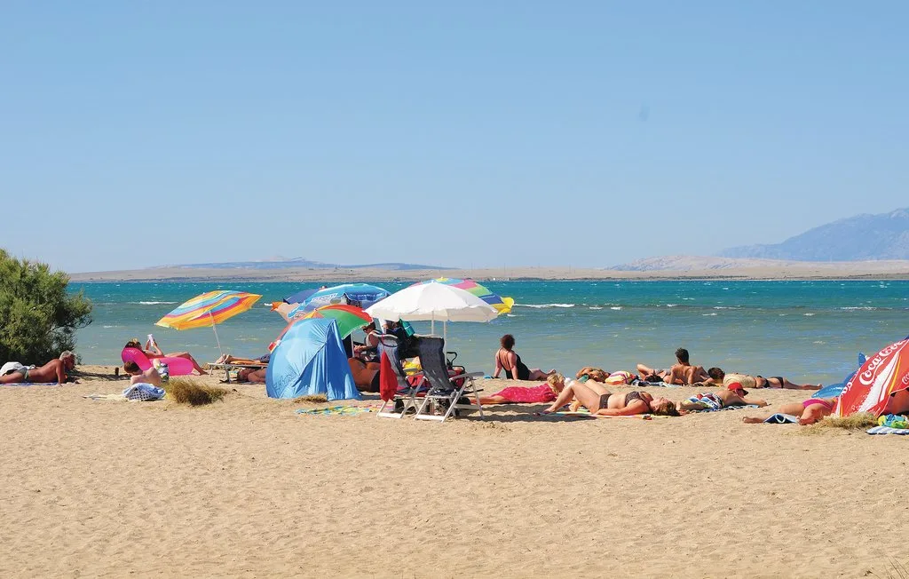 A sandy beach with sunbathers, colorful umbrellas, and blue water.