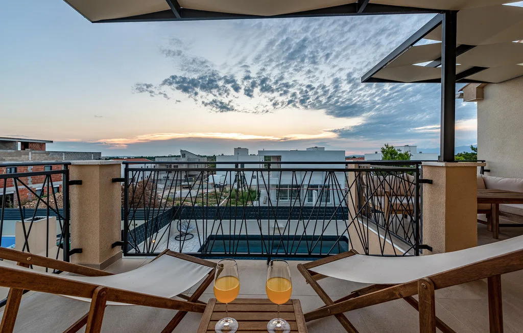 A terrace with lounge seating overlooks nearby buildings beneath a colorful sunset sky.
