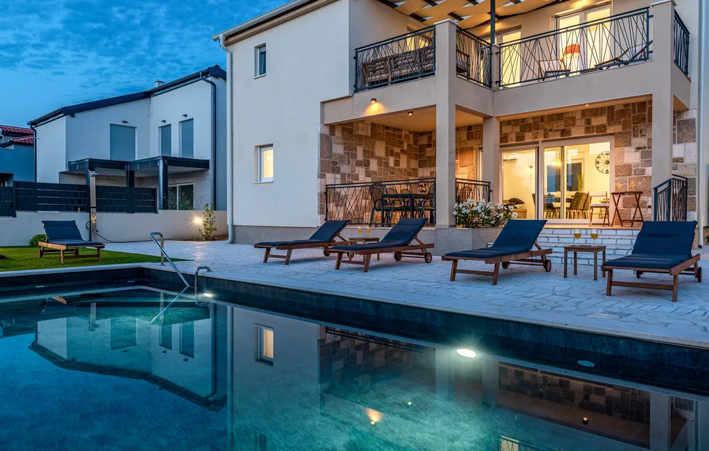 A modern house overlooks a swimming pool, with loungers on the surrounding patio.