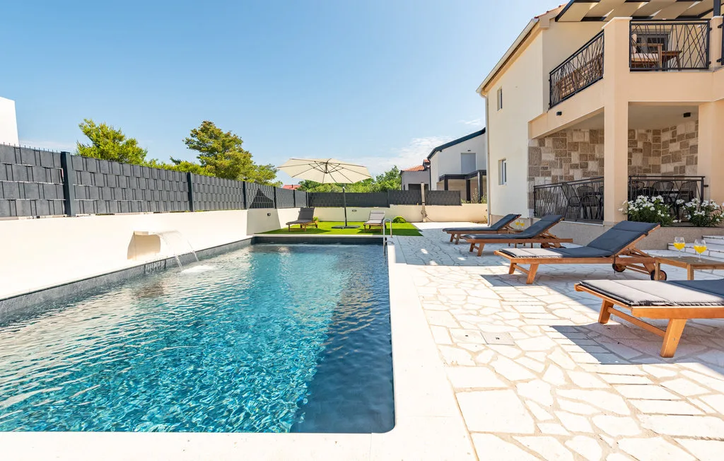 An outdoor swimming pool beside a paved patio with lounge seating.