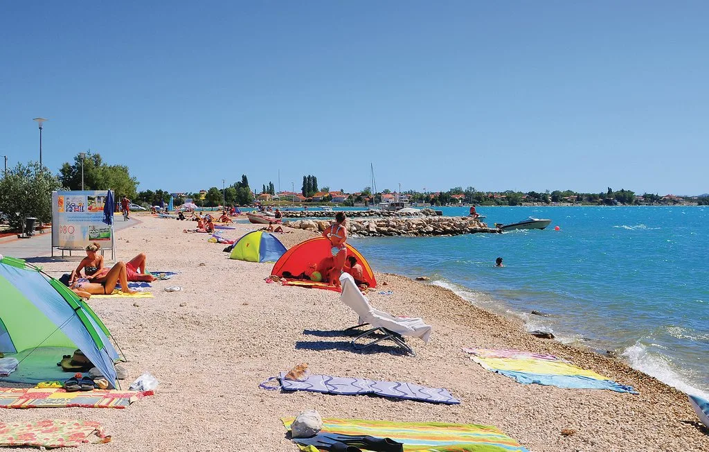 A sunny beach with people sunbathing on towels beside the blue sea.