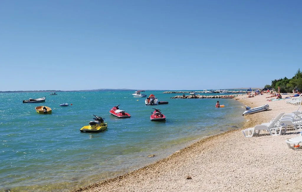 A sunny beach with boats and personal watercraft floating offshore.